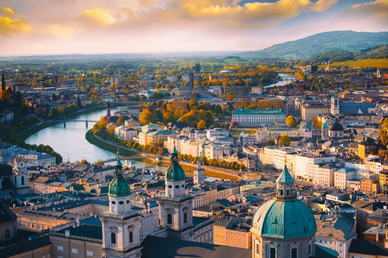 Vedere aeriană asupra Vienei, cu râul Dunărea traversând orașul și cupolele verzi ale Catedralei Sfântul Ștefan evidențiindu-se în peisaj.